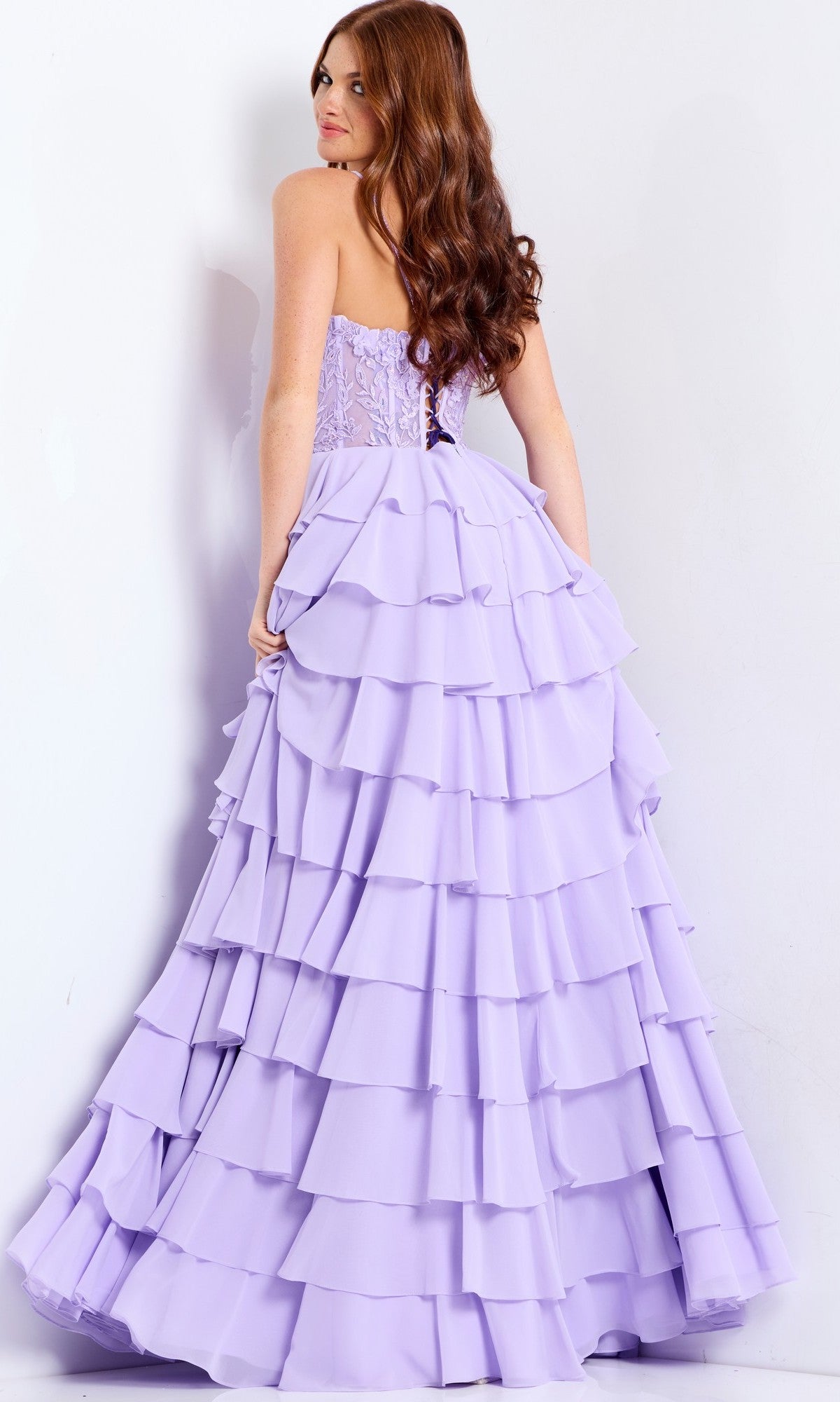 A woman with long, wavy auburn hair models the Jovani 44543 long prom dress, a strapless lavender gown with a corset bodice and layered ruffle chiffon skirt, against a plain white background.